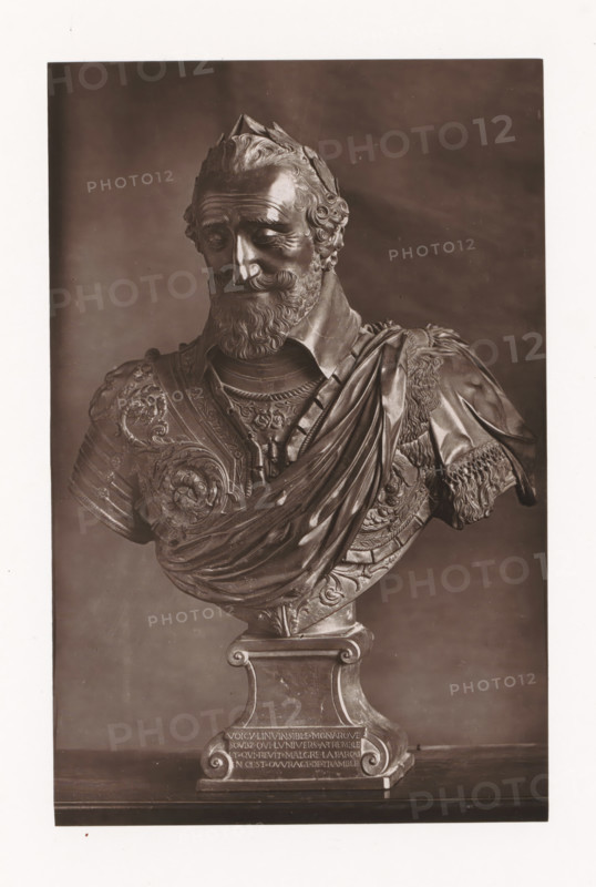 Bust of Henry IV of France, displayed during the Exposition Rétrospective of 1873 in Tours, France, page, photomechanical print, maker: Gabriel Blaise, Tours, 1873, paper, Woodburytype, Woodburytypie, height 195 mm x width 126 mm, Person, Henry IV (King of France and Navarre), piece of sculpture, reproduction of a piece of sculpture, temporary exhibition, 'Salon', Period, 1873-05-03 - 1873-05-25, A monochrome photograph of a sculpted bust showing a bearded man with curly hair and a laurel-like headpiece, wearing ornate armor and a draped cloak; the bust rests on a decorative pedestal with carved scroll details and a rectangular base, and the background is plain and darker than the sculpture.