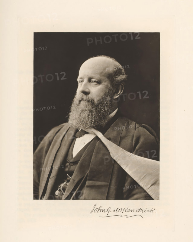 Portrait of John Gray McKendrick, John G. MKendrick, page, photomechanical print, cliché maker: T. & R. Annan & Sons, Glasgow, c. 1886 - in or before 1891, photographer, paper, photoaquatint, height 195 mm x width 147 mm, Print on fifth unnumbered page after page 128., Person, John Gray McKendrick, historical persons, physician, doctor, professor, A sepia-toned portrait of a middle-aged man shown from the chest up against a dark rectangular background, with a full beard and mustache, a high forehead with thinning hair, and a calm, forward-looking expression; he wears a dark formal coat and waistcoat over a white shirt with a bow at the collar, and a light-colored draped cloth across one shoulder, with a pocket watch chain visible at his vest.