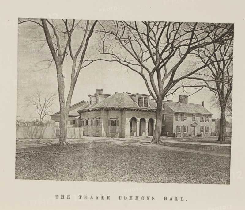 The Thayer Commons Hall, View of the Thayer Commons Hall of Harvard University, page, photomechanical print, c. 1870 - in or before 1875, paper, collotype, photoprint, height 156 mm x width 208 mm, university building, college, North America, Massachusetts, Cambridge (MA), Harvard College, A sepia-toned photograph showing a large house with a rounded central section featuring arched openings and shuttered windows, flanked by rectangular wings with multiple windows and a chimney; several tall leafless trees stand in front of the building, their bare branches extending across the sky and casting shadows on the ground, and a low fence runs beside one wing while a grassy lawn fills the foreground.
