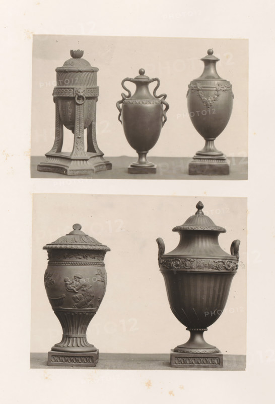 Five decorated vases, photograph, page, photographer: Joseph Cundall, c. 1868 - in or before 1873, paper, carbon print, height 361 mm x width 270 mm, sculpture (relief, sculpture), container of stone: stone vase, A photographic sheet showing two horizontal rows of classical urns and vases photographed against a plain light background, with three urns in the top row and two larger urns in the bottom row, each urn shown from the front. The top left urn has a tall covered body supported by a square pedestal with four ornate legs, a domed lid topped with a floral finial, and carved decorative bands and a lion-head ring detail. The top center urn is a slender covered vessel with a rounded body, a small stepped base, a lid with a rounded knob, and two sinuous handles that curve from the neck to the shoulder with a decorative band below the rim. The top right urn is an elongated covered vase on a square base with a flared neck, a domed lid topped with a small round finial, and a garland motif...