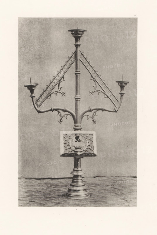 Easter candelabrum from the Saint-Vaast Church in Gaurain-Ramecroix, displayed at an exhibition of religious objects from the Middle Ages and Renaissance in 1864 in Mechelen, page, photomechanical print, number: '6 ...', number: '6', number: '-52', photographer: Joseph Maes, Mechelen, clichémaker: Simonau & Toovey, Antwerp, 1864 - in or before 1866, paper, photolithography, height 225 mm x width 141 mm, chandelier, candelabrum, Easter, Period, 1864, A tall ornate metal stand with a central vertical shaft and a stepped circular base supports branching curved arms and triangular decorative panels with fleur-de-lis and trefoil motifs, ending in shallow cup-like holders with spikes; a square panel with a circular carved emblem is mounted on the shaft above the base.