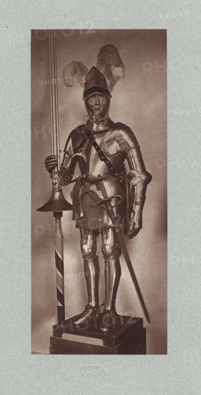 16th-century armor with lance and sword from the army of Henry II of France, from the collection of the Musée d'Artillerie in Paris, photomechanical print, This print is part of a cover with 36 prints, a title page and a list of images., check stamp: 'PHOTOGLYPTIE, LEMERCIER ET Cie, PARIS', Paris, cliché maker: Lemercier & Cie., c. 1877 - in or before 1882, Lemercier & Cie., photographer, cliché maker, paper, Woodburytype, Woodburytypie, height 275 mm x width 115 mm, hacking and thrusting weapons: sword, armour, helved weapons, polearms (for striking, hacking, thrusting): lance, A full-length figure in a suit of polished plate armor stands on a rectangular wooden pedestal, wearing a helmet with a pointed visor and large plume feathers rising above it, with a closed gauntleted hand gripping the shaft of a long pole weapon that rests on a circular guard, while the other hand hangs near the hilt of a sheathed sword at the waist; the armor includes articulated pauldrons, a breastplate with...