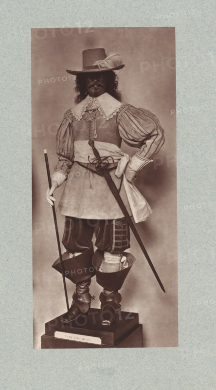17th-century uniform with sword from the army of Louis XIII of France, from the collection of the Musée d'Artillerie in Paris, photomechanical print, This print is part of a cover with 36 prints, a title page and a list of images., check stamp: 'PHOTOGLYPTIE, LEMERCIER ET Cie, PARIS', Paris, cliché maker: Lemercier & Cie., c. 1877 - in or before 1882, Lemercier & Cie., photographer, cliché maker, paper, Woodburytype, Woodburytypie, height 271 mm x width 123 mm, hacking and thrusting weapons: sword, (military) uniforms, A sepia-toned full-length portrait of a person standing on a wooden pedestal, wearing a wide-brimmed hat with a feather, a lace-trimmed collar over a fitted doublet with puffed, striped sleeves, and a sash tied at the waist; the figure holds a long thin staff in one gloved hand and a sheathed sword hangs at the hip, while the other hand rests on the waist; they wear knee-length breeches tucked into tall leather boots with turned-over tops and decorative spurs, and long h...