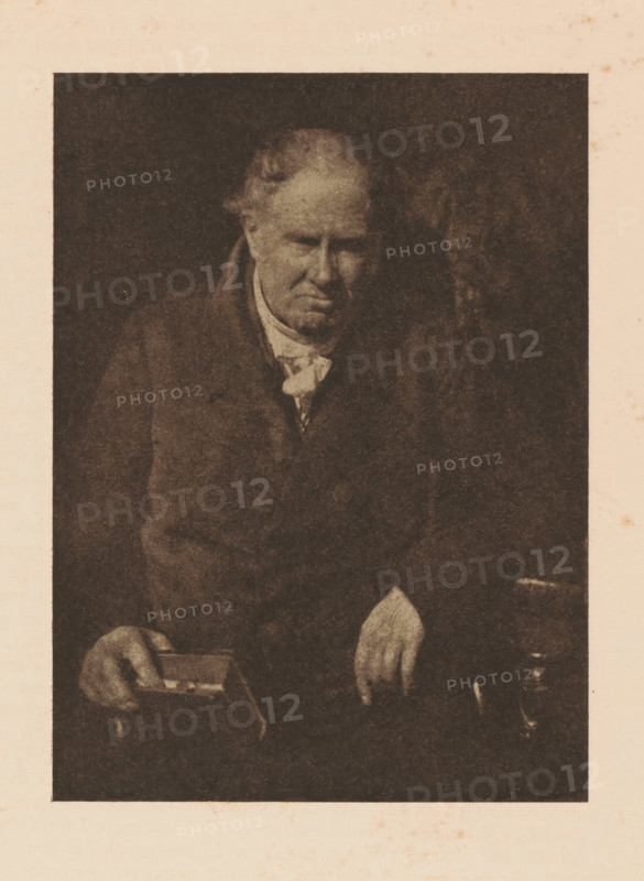 Portrait of Dr. Alexander Monro, page, photomechanical print, photographer: David Octavius Hill, cliché maker: anonymous, c. 1900 - in or before 1905, paper, autotypie, height 151 mm x width 111 mm, Person, Alexander Monro (III), historical persons, A sepia-toned portrait of an older man seated against a dark background, showing his upper body and hands; he wears a dark coat over a lighter shirt with a loosely tied neck cloth, his hair is thinning and receding at the temples, his face is downturned with a somber expression, one hand rests on a small rectangular box held in his lap while the other hand hangs over his knee, and a small jug-like object is visible near his right hand.