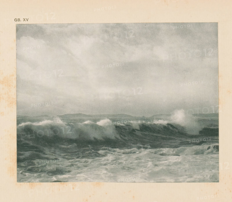 Seascape, page, photomechanical print, inscription: 'GB. XV.', monogram: 'AG', inscription: 'A wind sea by FJ Mortimer', photographer: Francis James Mortimer, cliché maker: anonymous, c. 1900 - in or before 1905, paper, autotypie, height 111 mm x width 141 mm, sea (seascape), A rectangular image shows a grayscale seascape with choppy waves in the foreground and a distant low horizon, topped by a cloudy sky; the surrounding area is a beige paper border with some uneven darker stains along the left and bottom edges.