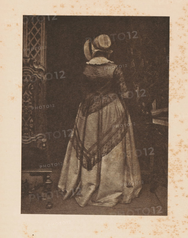Portrait of Mary Hamilton Ruthven, page, photomechanical print, photographer: David Octavius Hill, cliché maker: anonymous, c. 1900 - in or before 1905, paper, autotypie, height 152 mm x width 112 mm, Person, Mary Hamilton Ruthven, historical persons - BB - woman, A sepia-toned portrait of a woman seen from behind, wearing a floor-length dress with a patterned shawl draped over her shoulders and a small rounded hat; the dress has visible folds and vertical lines, and a ruffled collar is visible at the nape; ornate carved woodwork appears at the left edge and a dark interior fills the background.