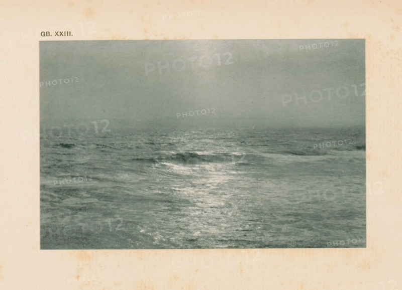 Seascape, page, photomechanical print, inscription: 'GB. XXIII.', inscription: 'Land & sea by WJ Day', photographer: William James Day, cliché maker: anonymous, c. 1900 - in or before 1905, paper, autotypie, height 92 mm x width 143 mm, sea (seascape), A rectangular photograph of a seascape showing a calm, expansive ocean with gentle waves and a reflective sheen on the water surface under a hazy sky, surrounded by a wide off-white paper border with light brown age spots.