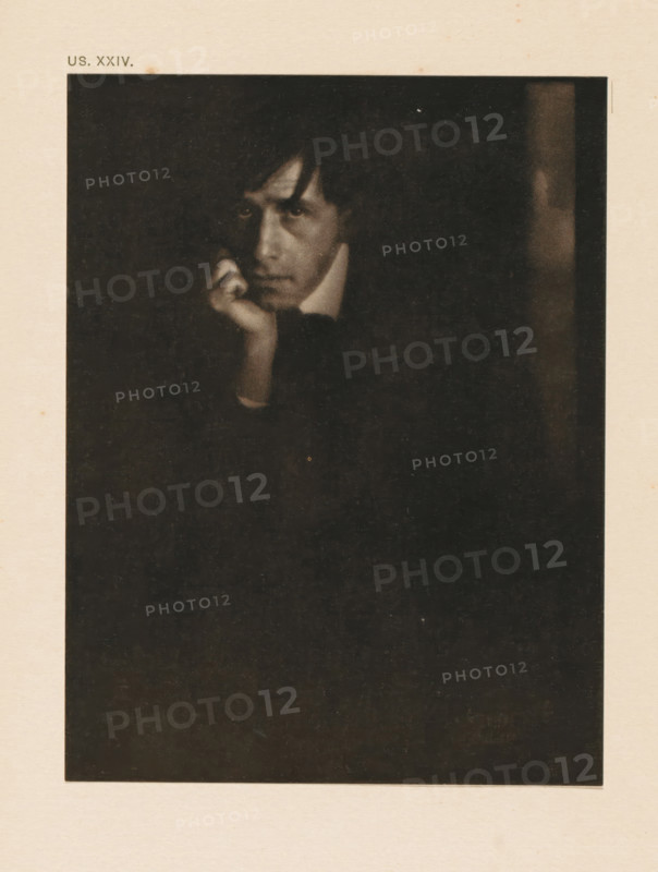 Portrait of Clarence Hudson White, page, photomechanical print, inscription: 'Portrait of Clarence H. White by Eduard J. Steichen', inscription: 'US. XXIV.', photographer: Edward Steichen, cliché maker: anonymous, c. 1900 - in or before 1905, paper, two-color autotype, height 149 mm x width 114 mm, Person, Clarence Hudson White, historical persons, portrait, self-portrait of photographer, A dark, grainy portrait of a person with a pale face partially lit against a black background, the person resting their chin on a hand with fingers near the mouth, short dark hair with a fringe falling toward the forehead, a visible high collar and a contemplative facial expression, framed by a wide pale border.
