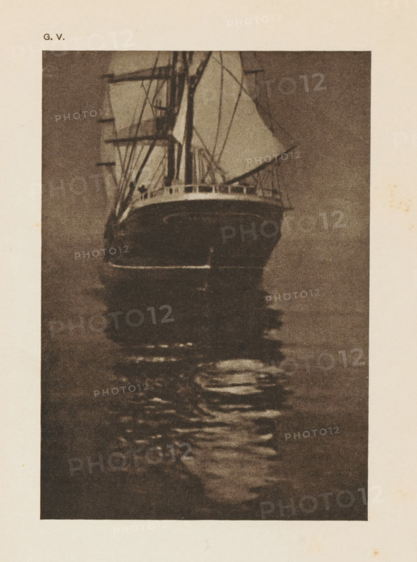Rear of a sailing ship, page, photomechanical print, inscription: 'A calm sea by O. Hofmeister', inscription: 'GV', photographer: Oskar Hofmeister, cliché maker: anonymous, c. 1900 - in or before 1905, paper, autotypie, height 151 mm x width 106 mm, sailing-ship, sailing-boat, A tall sailing ship seen from the front with masts, spars, and rigging, sails partially furled, a visible deck rail, and the ship’s dark hull reflected in rippling water below, all shown in a grainy, monochrome print on a pale background.