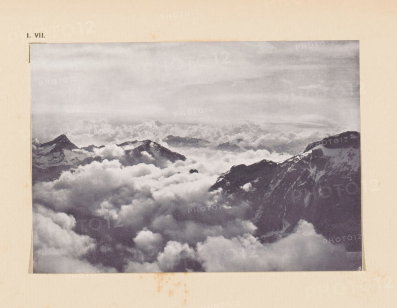 View of the Graian Alps, page, photomechanical print, inscription: 'I. VII.', inscription: 'Clouds Graian Alps by V. Sella', photographer: Vittorio Sella, Graian Alps, cliché maker: anonymous, c. 1900 - in or before 1905, paper, autotypie, height 100 mm x width 143 mm, mountain-range, snow peaks, A sepia-toned photograph mounted on aged paper shows a high-altitude mountain scene with rugged peaks rising above a vast sea of billowing clouds, darker rocky ridges with patches of snow visible near the right edge, softer distant summits partially obscured by mist, and a broad textured sky above the cloud layer.