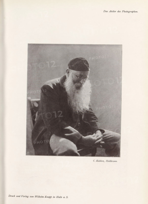 Portrait of an unknown man, page, photomechanical print, inscription: 'Das Atelier des Photographen.', monogram: 'LEIPZIG, S G', photographer: Curt Kubica, Heilbronn, cliché maker: unknown, Leipzig, printer (person): Wilhelm Knapp, Halle an der Saale, c. 1895 - in or before 1900, printer (person), Baden-Württemberg, Saxony-Anhalt, Saxony, paper, autotypie, height 142 mm x width 120 mm, historical persons, A grayscale photograph of an elderly man seated and leaning forward, wearing a dark cap and a dark jacket, with a long white beard flowing over his chest; his head is bowed and his eyes are partly obscured by glasses, his hands rest together in his lap, and a simple chair back is visible behind him against a plain background.