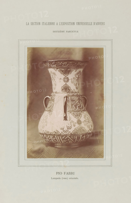 Decorated vase, Pio Fabri - Lampada (vaso) orientale, La Section Italienne a l'Exposition Universelle d'Anvers - Deuxième Fascicule, photograph, page, c. 1880 - in or before 1885, photographer, paper, albumen print, height 138 mm x width 95 mm, Photo on loose plate opposite page 36., container of ceramics: jar, jug, pot, vase, A sepia-toned photograph of a decorative vase centered within a bordered page, showing a flared neck, rounded body, two small looped handles, and a vertical spout-like projection from the neck area; the vase surface is covered in intricate repeating floral and geometric patterns and ornate bands around the neck and base, with contrasting darker decorative motifs against a lighter background; the vase rests on a textured cloth and is framed by multiple thin rectangular lines on the page.