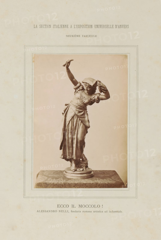 Sculpture of a woman, Ecce il Moccolo!, La Section Italienne a l'Exposition Universelle d'Anvers - Deuxième Fascicule, photograph, page, inscription: 'ALESSANDRO NELLI, fonderia romana artistica ed industriale.', c. 1880 - in or before 1885, photographer, paper, albumen print, height 138 mm x width 97 mm, Photo on loose plate opposite page 48., piece of sculpture, reproduction of a piece of sculpture, adult woman, A framed sepia photograph of a sculpted female figure standing on a decorative round base placed on a patterned cloth, the woman wearing a flowing dress with gathered sleeves and a sash at the waist, one arm raised holding a small object and the other bent with a hand near her head, a cloth or headscarf partially covering her hair, detailed drapery in the skirt and visible footwear on the base, the photograph mounted on a textured sheet with a visible border around the image.