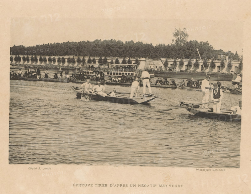 Rowers with spectators on the rowing course, page, photomechanical print, inscription: 'Épreuve tirée d'après un négatif sur fout', photographer: Albert Londe, cliché maker: Michel Berthaud, c. 1883 - in or before 1888, Albert Londe, Michel Berthaud, photographer, cliché maker, paper, collotype, photoprint, height 103 mm x width 160 mm, rowing, canoeing, etc. (sport) (organization, club (sports, games, etc.)), A wide waterscape shows multiple rowboats and small vessels clustered on a calm river, each boat occupied by people wearing light-colored clothing and dark vests, some standing and some seated while holding oars or leaning on boat edges; in the foreground a few boats are closer with visible water ripples and gentle waves, while behind them a larger passenger boat and more crowded small craft line the river near a stone embankment topped by a balustrade and a row of evenly spaced trees; beyond the embankment dense foliage and taller trees rise against a pale sky, and along the riv...