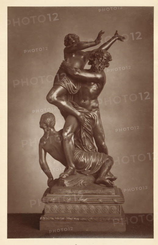 Bronze statue of the robbery of Proserpina, from the collection of Christopher Beckett Denison, page, photomechanical print, number: '805', c. 1880 - in or before 1885, paper, Woodburytype, height 194 mm x width 122 mm, Print on third unnumbered page after page 78., the rape of Proserpina (by Pluto in his chariot), possibly with Diana and Minerva trying to rescue her, piece of sculpture (precious metals, arts), A monochrome photograph of a multi-figure sculpture mounted on a decorative rectangular pedestal, showing three intertwined human figures rendered in a smooth, reflective material. One figure stands centrally, muscular with a bearded face turned sideways and arms lifting another figure who is elevated with arms raised and head tilted back, torso partially draped. A third figure kneels at the base, turned away with hair gathered at the nape and one arm extended downward, supporting the composition. Drapery folds wrap around hips and legs of the figures, and the pedestal features ...