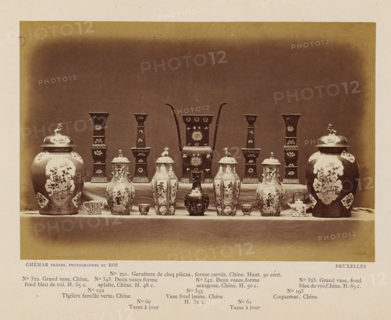 Sixteen objects, including Chinese vases, photograph, page, inscription: 'No. 322. Grand vase, Chine, fon bleu de roi. H. 65 c., ', photographer: Ghémar Frères, c. 1870 - in or before 1875, paper, albumen print, height 122 mm x width 180 mm, container of ceramics: jar, jug, pot, vase, A symmetrical arrangement of ceramic and metal vessels sits on a draped table against a plain dark backdrop, including two large lidded urns with painted floral panels positioned at the outer edges, pairs of tall hexagonal vases with ornate surface decoration set inward from the urns, several lidded baluster-shaped jars with decorative scenes and finial handles across the front, a central tall rectangular vessel with curved handles rising from its sides and floral motifs, smaller cups and a small lidded box placed between the larger pieces, and a narrow foreground strip of lighter surface separating the display from the backdrop.