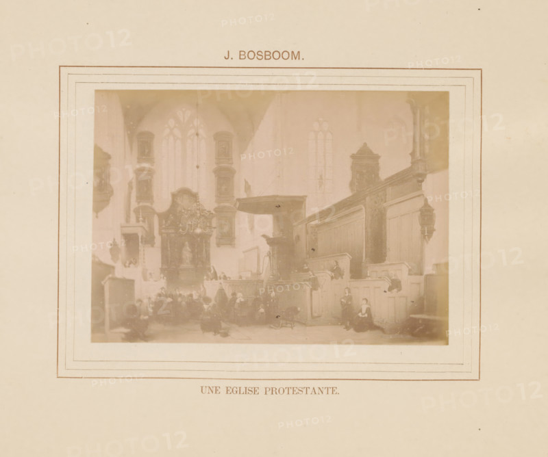 Une eglise protestante, Photo reproduction of Une eglise protestante by Johannes Bosboom, photograph, reproduction, page, inscription: 'J. Bosboom', after painting by Johannes Bosboom, c. 1878 - in or before 1883, photographer, paper, albumen print, height 92 mm x width 128 mm, interior of church, painting, drawing and the graphic arts, A faded photographic print mounted on a larger sheet with a rectangular decorative border, showing an interior scene with tall arched windows, wooden paneling, elevated pulpit area, ornate altarpiece with a statue, hanging chandelier, several seated and standing figures wearing period clothing, and muted sepia tones throughout.