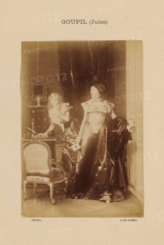 Goupil (Jules), Photo reproduction of La Lettre by Jules Adolphe Goupil, photograph, reproduction, page, photographer: Alexandre, after painting by Jules Adolphe Goupil, c. 1888 - in or before 1893, paper, albumen print, albumendruk, height 144 mm x width 101 mm, adult man, painting, drawing and the graphic arts, A sepia-toned photograph shows two women in elaborate period dresses standing in an interior with paneled walls and heavy drapery. One woman stands facing slightly sideways wearing a long, glossy skirt, a fitted bodice with decorative details, and a small hat, holding a folded card in one hand and a dark cloak draped over her other arm. The other woman leans on a small table while looking toward the first woman; she wears a ruffled collar and a dress with puffed sleeves and is positioned beside a decorative chest topped with an ornate framed mirror and a vase. In the foreground there is an upholstered chair with curved wooden legs and carved details, and the floor shows a patt...