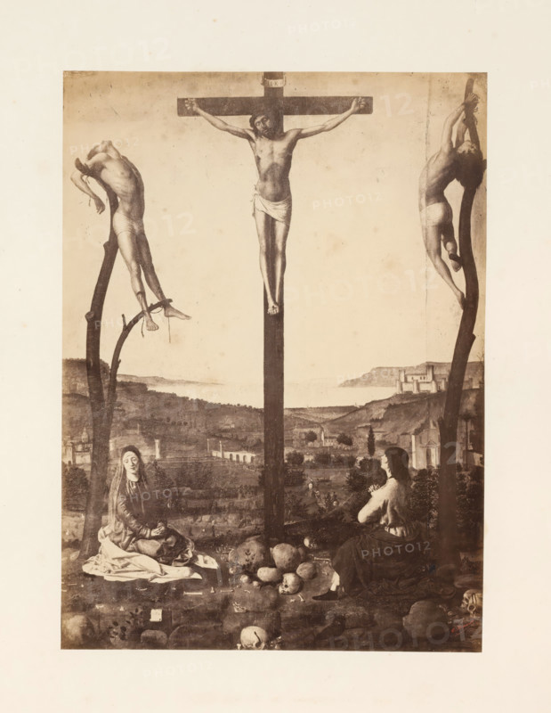 Photo reproduction of the Crucifixion of Christ by Antonello da Messina, photograph, reproduction, page, photographer: Edmond Fierlants, after painting by Antonello da Messina, publisher: C. Muquardt, Brussels, c. 1856 - in or before c. 1861, paper, albumen print, albumendruk, height 370 mm x width 269 mm, crucified Christ, with particular persons under the cross, A sepia-toned depiction of a crucifixion scene framed by a pale border, showing a central wooden cross with a male figure suspended, arms outstretched and a cloth around his waist, flanked by two other wooden supports each bearing a male figure in contorted poses with minimal clothing. Below the crosses, a rocky foreground contains scattered skulls and stones, and two seated women in long draped garments face the central cross, one with hands clasped and the other looking downward. In the middle distance there is a gently rolling landscape with buildings and a coastline visible under a soft, light sky.