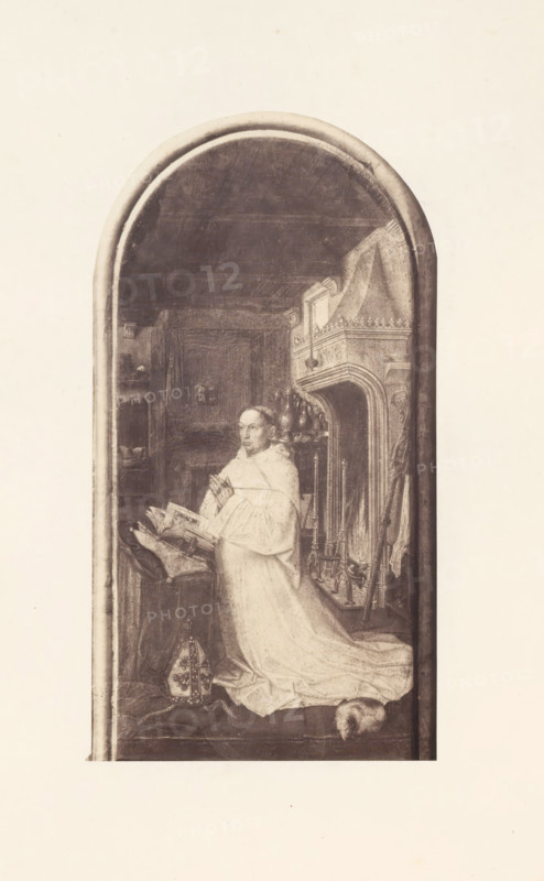 Photo reproduction of Christiaan de Hondt, abbot of Ter Duinen, photograph, reproduction, page, photographer: Edmond Fierlants, after painting by anonymous, publisher: C. Muquardt, Brussels, c. 1856 - in or before c. 1861, paper, albumen print, albumendruk, height 317 mm x width 168 mm, monk(s), friar(s), one person praying, A tall, narrow arched panel shows a robed figure kneeling in front of an open book on a lectern, hands clasped in a prayer gesture and gaze directed slightly upward; the figure wears a flowing light-colored robe with a long train spread on the floor and a cap placed near the feet. To the right of the figure is an ornate carved fireplace with decorative mantelshelf details and a set of andirons and tools leaning nearby, while behind and above the figure shelves, drapery, and architectural moldings are visible in dim tones. The scene is rendered in muted monochrome tones and framed by a rounded arch border with a plain lighter background surrounding the panel.