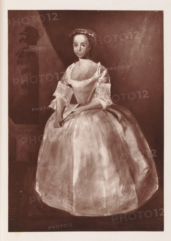 Photo reproduction of a painting depicting a portrait of Grace Naylor, reproduction, page, photomechanical print, cliché maker: Woodbury Permanent Photographic Printing Company, after painting by anonymous, c. 1866 - in or before 1876, photographer, paper, Woodburytype, height 132 mm x width 92 mm, Person, Grace Naylor, adolescent, young woman, maiden, historical persons (portraits and scenes from the life), A sepia-toned portrait of a woman standing and facing forward, wearing a wide, full skirt dress with a low neckline and short, ruffled sleeves; her hands are clasped at waist level, one hand holding a folded fan, and she has a calm, neutral facial expression with hair pulled back and a headband or small cap. The background is dark and plain with a lighter triangular area behind her and a darker vertical rectangular panel to her left that contains a shadowy silhouette resembling a carved or painted figure. The image has a narrow light border around the portrait and a slightly textur...