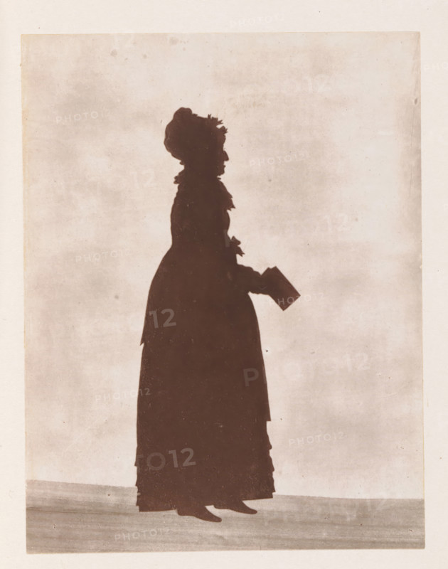 Photo reproduction of a drawing depicting a silhouette of Anna Maria Shipley, reproduction, page, photomechanical print, cliché maker: Woodbury Permanent Photographic Printing Company, after drawing by anonymous, c. 1866 - in or before 1876, photographer, paper, Woodburytype, Woodburytypie, height 118 mm x width 91 mm, silhouette-apparatus, 'physionotrace', A side silhouette of a standing person wearing a long dress and a hat with decorative elements, holding a small rectangular object in one gloved hand, with visible shoes at the hem, all set against a plain, lightly textured background.