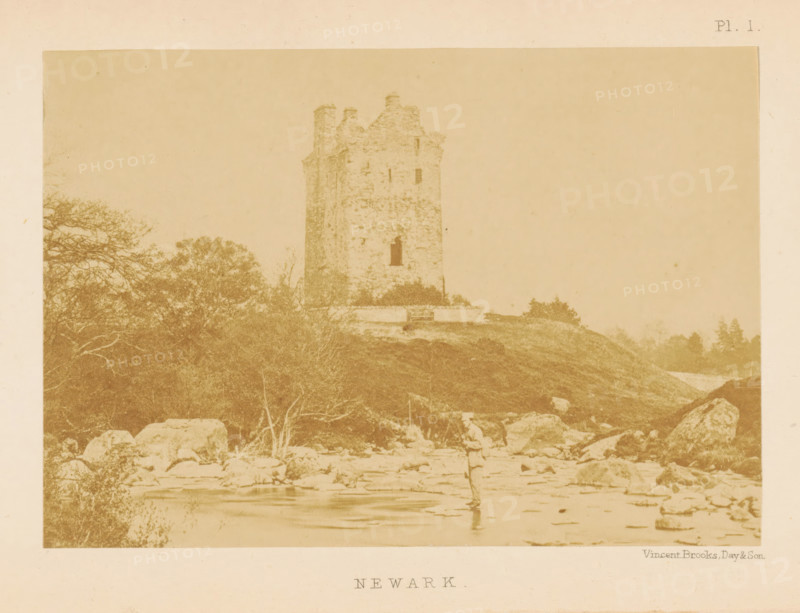 Newark, View of the ruins of Newark Castle, photograph, page, number: 'Pl. 1.', photographer: Vincent Brooks, Day & Son, Newark Castle, c. 1864 - in or before 1874, North America, paper, albumen print, height 85 mm x width 121 mm, Photo opposite title page., landscape with ruins, ruin of a dwelling, house, castle, A sepia-toned photograph showing a stone tower on a grassy hill with surrounding trees and rocky foreground, a solitary figure standing in shallow water near the rocks, and scattered boulders and vegetation across the scene.