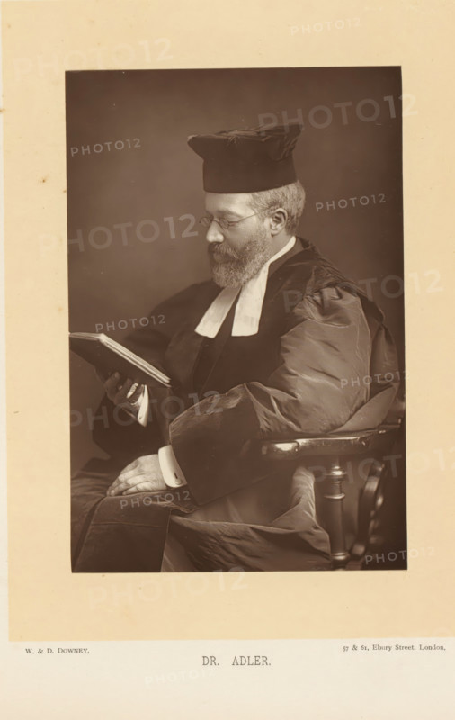 Dr. Adler, Portrait of Hermann Adler, reading a book, page, photomechanical print, inscription: '57 & 61, Elbury Street, London.', photographer: Downey, William & Daniel, London, cliché maker: anonymous, c. 1882 - in or before 1892, paper, Woodburytype, height 139 mm x width 93 mm, Person, Hermann Adler, reading, chief rabbi, A sepia-toned portrait of a bearded man seated in a wooden armchair, wearing dark academic robes with light-colored bands at the collar and a square cap, looking down at an open book held in one hand while the other hand rests on his lap; the image is bordered by a wide pale margin.