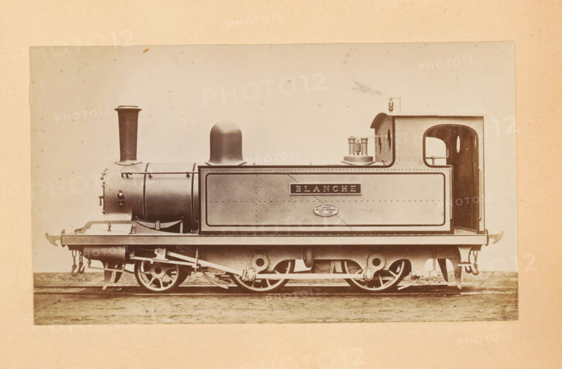 Passenger steam locomotive made by Sharp, Stewart and Company, photograph, page, inscription: 'Class 816. Passenger tank engine', c. 1874 - in or before 1884, photographer, paper, albumen print, height 83 mm x width 143 mm, steam locomotive, A sepia-toned photograph of a small steam locomotive shown in profile on a pale background, with a cylindrical boiler and a tall narrow chimney at the front, a rounded dome midway, and a rectangular tank section behind with riveted metal panels. The locomotive sits on visible driving wheels and connecting rods beneath a flat running plate, with exposed mechanical linkages and suspension elements. At the rear there is an open cab with a rounded doorway and a small handrail, and on the top of the tank near the cab are cylindrical fittings and a rectangular raised housing. The image has a textured paper border and small specks and blemishes across the background.