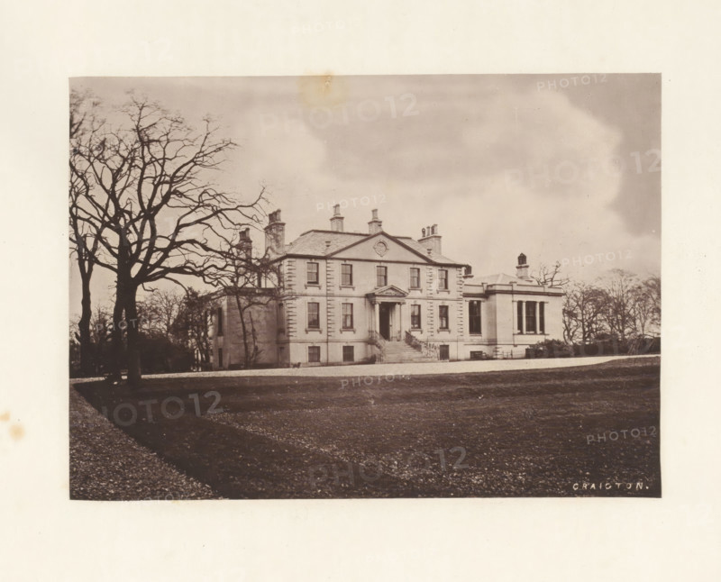 Craigton, photograph, page, photographer: Thomas Annan, Scotland, c. 1868 - in or before 1878, paper, carbon print, height 115 mm x width 160 mm, rural housing, eg country-house, villa, cottage, façade (or house or building), A large classical house with a symmetrical façade and a central pediment sits on a raised terrace with a flight of steps leading to an entrance with columns, flanked by tall windows and chimneys on the roof; a bare-branched tree is prominent in the foreground to the left, casting a shadow across a gravel drive and a lawn that stretches toward the house, while additional leafless trees frame the scene against a cloudy sky.