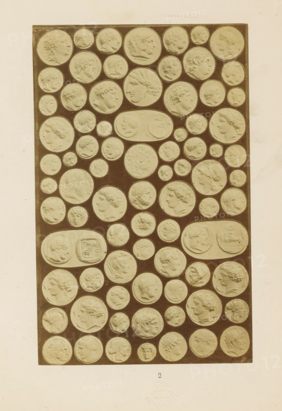 Antique medals, photograph, page, number: '2', name: 'A. Cadart 3. Rue St. Fiacre Paris Editeur', Rome, c. 1849 - in or before 1859, photographer, paper, albumen print, height 199 mm x width 126 mm, medal (considered as a piece of sculpture, regardless of its specific function), A tall rectangular panel filled with many circular and oval medallions set against a dark background, each medallion containing a raised profile or bust of a face in various orientations and styles, mostly shown in light beige relief against the darker panel, arranged in tight rows with small gaps between them, the panel centered on a larger light-colored page with a faint circular embossed mark near the lower edge.