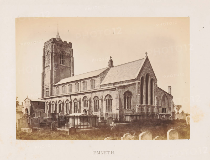 Emneth, photograph, page, photographer: Edward Johnson, c. 1858 - in or before 1869, Norfolk (county), paper, albumen print, height 126 mm x width 178 mm, church (exterior), facade (of house or building), churchyard (around church), Saint Edmund's Church (Emneth), A sepia-toned photograph of a large stone church with a tall square tower topped by a small spire and crenellated parapet, a long nave with rows of tall arched windows, and a pitched roof with decorative finials; in front of the church is a graveyard with numerous headstones of various shapes and a fenced tomb with vertical bars; the image is bordered by a wide pale margin.