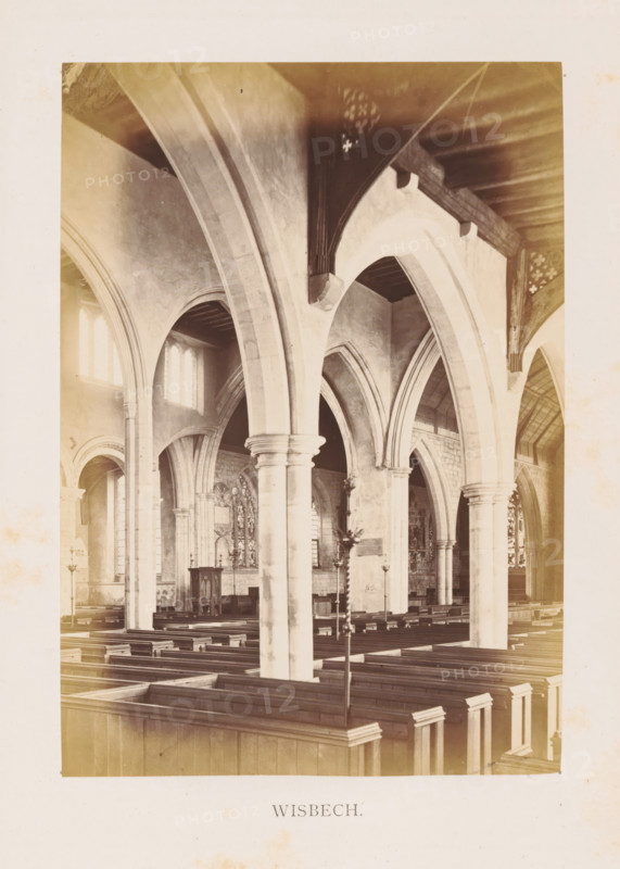 Wisbech, photograph, page, photographer: Edward Johnson, Parish Church of Saint Peter and Paul, c. 1858 - in or before 1869, Cambridgeshire, paper, albumen print, height 177 mm x width 125 mm, interior of church, parts of church interior: aisle, The image shows the interior of a church with tall stone arches and columns supporting a wooden ceiling, rows of wooden pews filling the nave, arched windows admitting light into the space, ornate stonework and carved details around the arches, a pulpit or lectern set against a wall with decorative panels and stained glass visible in the background, and a freestanding metal candleholder or stand positioned among the pews.