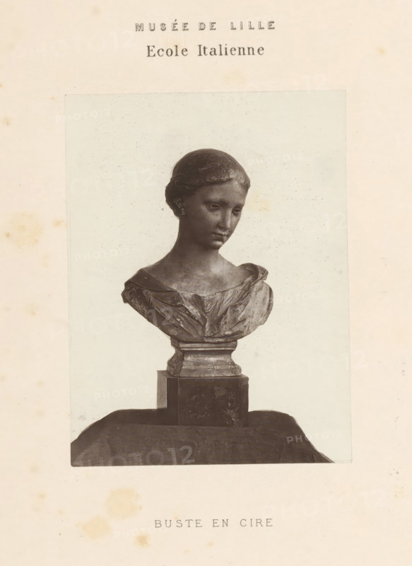 Wax bust of a woman, Bust en cire, page, photomechanical print, inscription: 'Musée de Lille Ecole Italienne', Lille, printer (person): Goupil & Cie., c. 1862 - in or before 1872, printer (person), paper, Woodburytype, height 117 mm x width 88 mm, Print opposite title page., chest, bust - AA - female human figure, A photographic print of a sculpted bust of a young woman mounted on a pedestal, shown from the shoulders upward, with her head slightly tilted and hair styled close to the head; the bust displays a draped garment across the shoulders and chest, and the pedestal has a stepped rectangular base sitting on a draped cloth surface, all presented against a pale background within a border on an aged, slightly spotted paper.