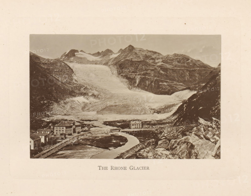 The Rhone Glacier, View of the Rhône Glacier in Switzerland, page, photomechanical print, Switzerland, c. 1874 - in or before 1884, paper, collotype, photoprint, height 86 mm x width 132 mm, glacier, Rhône glacier, A sepia-toned landscape photograph shows a wide glacial valley flanked by steep rocky mountains with snow and ice on their upper slopes, a broad ice flow descending toward the foreground, a winding river or meltwater stream running through the valley, scattered rocks and boulders on the slopes, and several multi-story buildings near the riverbank with pitched roofs and rectangular windows.