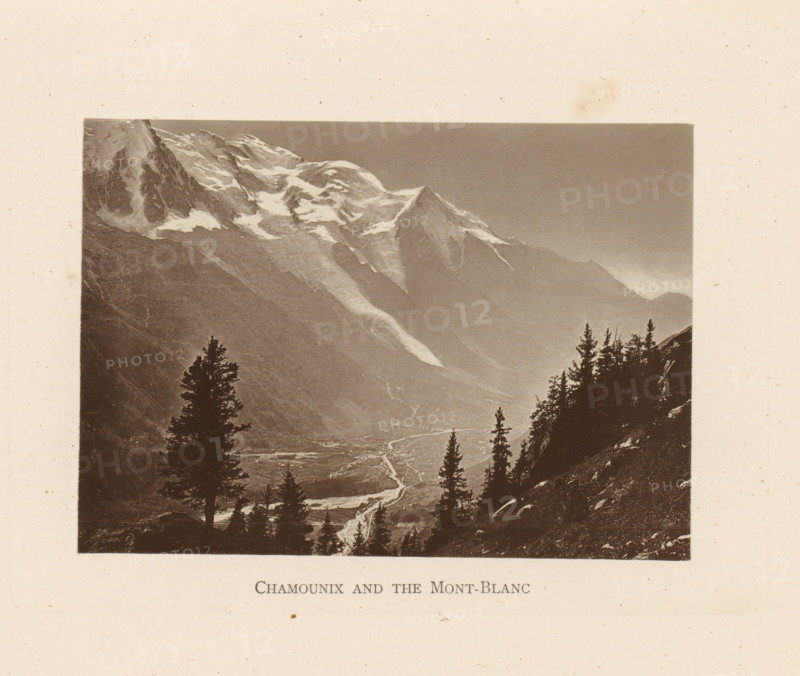 Chamounix and the Mont-Blanc, View of Chamonix and the Mont Blanc, page, photomechanical print, Chamonix, c. 1874 - in or before 1884, paper, collotype, photoprint, height 92 mm x width 129 mm, city-view in general, 'veduta', mountains, Mont Blanc, A sepia-toned landscape photograph shows a mountain range with snow patches on jagged peaks and steep slopes, a valley below with a winding river visible as a lighter ribbon, and dark silhouettes of tall evergreen trees in the foreground on a rocky hillside, all framed by a light textured border.