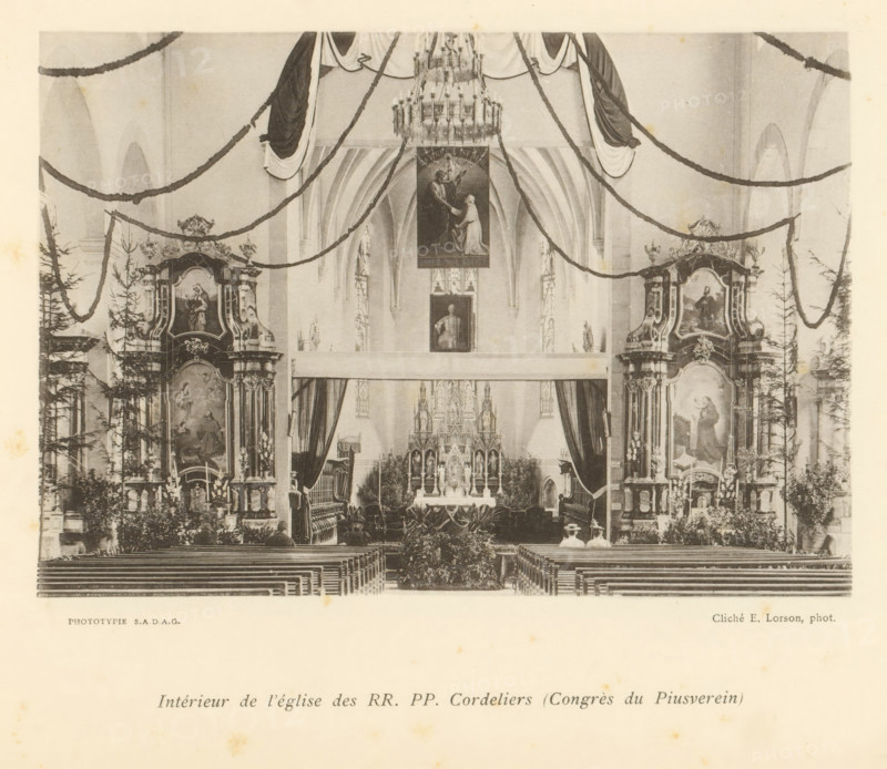 Interior of the L'Eglise des Cordeliers in Fribourg, Intérieur de l'église des RR. PP. Cordeliers (Congès du Piusverein), page, photomechanical print, maker: Ernest Lorson, Fribourg, maker: SADAG, 1897, paper, collotype, photoprint, height 111 mm x width 162 mm, interior of church, A black-and-white photograph of a church interior showing a central altar framed by ornate side altarpieces and tall arched ceilings, with garlands draped across the nave and a large chandelier hanging above; rows of wooden pews lead toward the altar, flanked by decorative columns, statues, paintings within carved frames, and potted plants, while curtains and an elaborately detailed reredos occupy the area behind the altar and two small figures are seated near the front pews.
