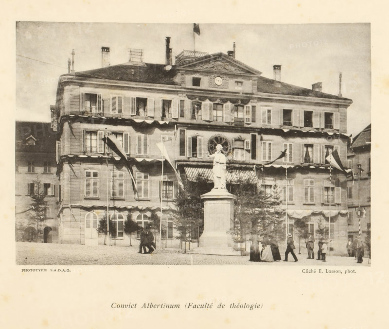 Convict Albertinum (Faculté de théologie), View of the Albertinum on the Square des Places in Fribourg, page, photomechanical print, photographer: Ernest Lorson, Fribourg, maker: SADAG, 1897, paper, collotype, light pressure, height 111 mm x width 162 mm, square, circus, university, A wide façade of a multi-story stone building with many shuttered windows and decorative molding spans the image, a flag flying atop its roof and several chimneys and rooftop structures visible; a statue of a robed figure stands on a tall pedestal in front of the building, surrounded by flagpoles with banners and awnings over ground-floor windows; cobblestone pavement fills the foreground where groups of people in period clothing are walking and standing, and small trees and architectural details frame the scene.