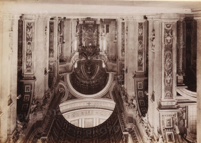 Interior of St. Peter's Basilica in Vatican City, photograph, page, Vatican City, c. 1850 - in or before 1860, photographer, paper, albumen print, height 97 mm x width 135 mm, interior of church, St. Peter's Basilica, An inverted sepia photograph showing an ornate interior with tall fluted columns and decorative pilasters, each panel embellished with carved figures and circular medallions; a large coffered dome with concentric decorative rings and sculptural details dominates the central area, framed by archways and richly patterned cornices; elaborate reliefs and statues sit atop ledges and niches, and decorative mouldings and geometric panels cover the walls and arches, all rendered in varying tones of brown and beige.