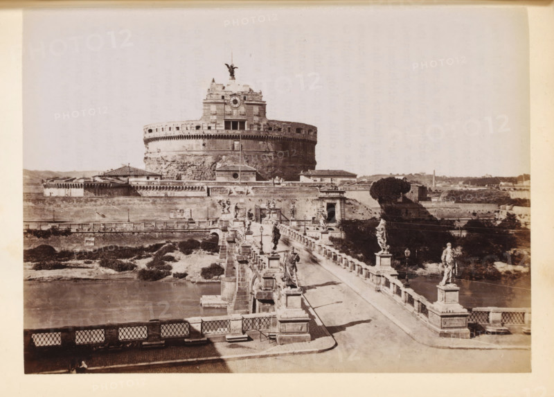 View of the Bridge of Angels and the Castel Sant'Angelo in Rome, photograph, page, Rome, c. 1850 - in or before 1860, photographer, paper, albumen print, height 98 mm x width 135 mm, bridge in city across river, canal, Engelenburcht, Engelenbrug, A wide sepia-toned photograph shows a large circular stone fortress with battlements and a tiered upper structure topped by a winged statue; a bridge lined with stone balustrades and multiple classical statues and lamp posts leads toward the fortress across a body of water, with walkways, stone pedestals, and shadowed figures visible on the bridge; surrounding the fortress are low buildings, walls, and grassy embankments, and a distant landscape of low hills and scattered structures forms the background.