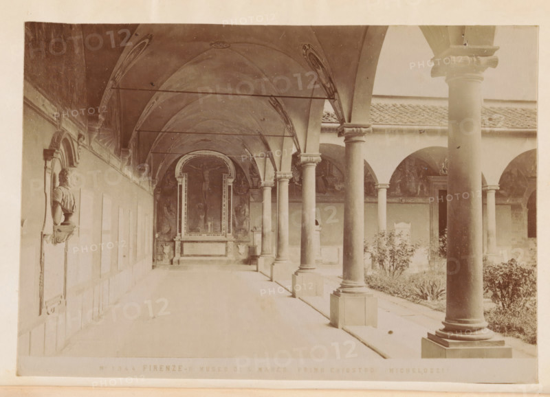 Firenze - Museo di S. Marco. primo chiostro (Michelozzi), Cloister of the San Marco Monastery in Florence, photograph, page, number: 'No 1344', Florence, c. 1880 - in or before 1890, photographer, Tuscany, paper, albumen print, height 97 mm x width 140 mm, cloisters, monastery, San Marco, A long, covered stone walkway lined with tall round columns supporting arches and a vaulted ceiling with decorative painted ribs runs beside a courtyard with plants and low walls; along the left wall a sculpted bust set in a framed niche is mounted above a small pedestal, and at the far end of the walkway a framed altar or niche with sculpted figures and ornate borders is visible beneath the vaulted arch.