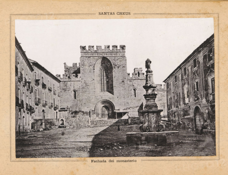 Facade of the Monastery of Santes Creus in Aiguamúrcia, Fachada del monasterio, Santas Creus, page, photomechanical print, Aiguamúrcia, c. 1874 - in or before 1884, Catalonia, paper, collotype, photoprint, height 111 mm x width 161 mm, abbey, monastery, convent, Roman Catholic church, Monastery of Santes Creus, A black and white photograph shows a stone plaza framed by buildings on both sides and a large medieval church or monastery facade in the center with a tall arched window and a rounded main doorway set into thick stone walls topped with crenellations; in front of the building a multi-tiered ornamental fountain with sculpted details stands on a circular basin, and steps lead up to the entrance; flanking the plaza are multi-story buildings with rows of windows and balconies on the left and a decorated facade with ornate window surrounds on the right; the ground appears uneven and worn, and the image is bordered by a textured paper frame.