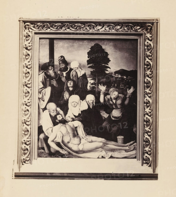 Photographic reproduction of a painting of the Descent from the Cross of Christ, possibly by Matthias Grünewald, photograph, reproduction, page, photographer: Gysi, after painting by Matthias Grünewald (possibly), c. 1856 - in or before 1866, paper, albumen print, height 132 mm x width 119 mm, picture, painting, Christ is laid down, descent from the cross, A framed rectangular painting with an ornate carved frame surrounding a scene of multiple figures clustered around a lifeless male figure lying on a draped surface, the central figure nude from the waist up with arms and legs extended, nearby figures wearing head coverings and robes with varied expressions and gestures, one woman raising her hands, another supporting the head of the fallen man, a bearded man and other attendants grouped at the upper left, a tree and distant landscape visible in the background, and a patterned cylindrical container near the feet of the central figure.