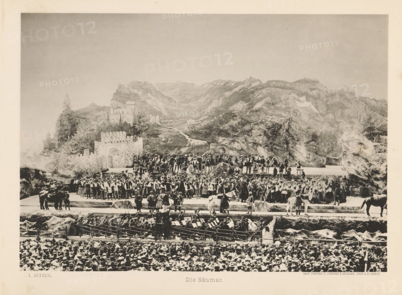 Die Säumer, View of a parade of mule drivers during the Calven-Feier in Chur, page, photomechanical print, number: 'I.', photographer: Lienhard & Salzborn, Chur, in or after 1899-05-28 - in or before 1899-06-04, paper, collotype, photoprint, height 178 mm x width 254 mm, mule, mountains, activities in the air, public festivities, eg fly-past, A wide sepia-toned scene shows a large outdoor stage set against a painted mountainous backdrop with rocky peaks and a winding valley. On the stage a dense group of people wear period costumes with varied styles including tunics, vests, capes, and hats, some holding staffs or musical instruments and a few positioned on raised platforms. Stone-like set pieces, walls, and faux vegetation frame parts of the stage, and several horses and riders stand near the edges. In front of the stage rows of seated audience members with many hats are visible, and an orchestra pit with musicians and music stands occupies the area between the stage and the audience....