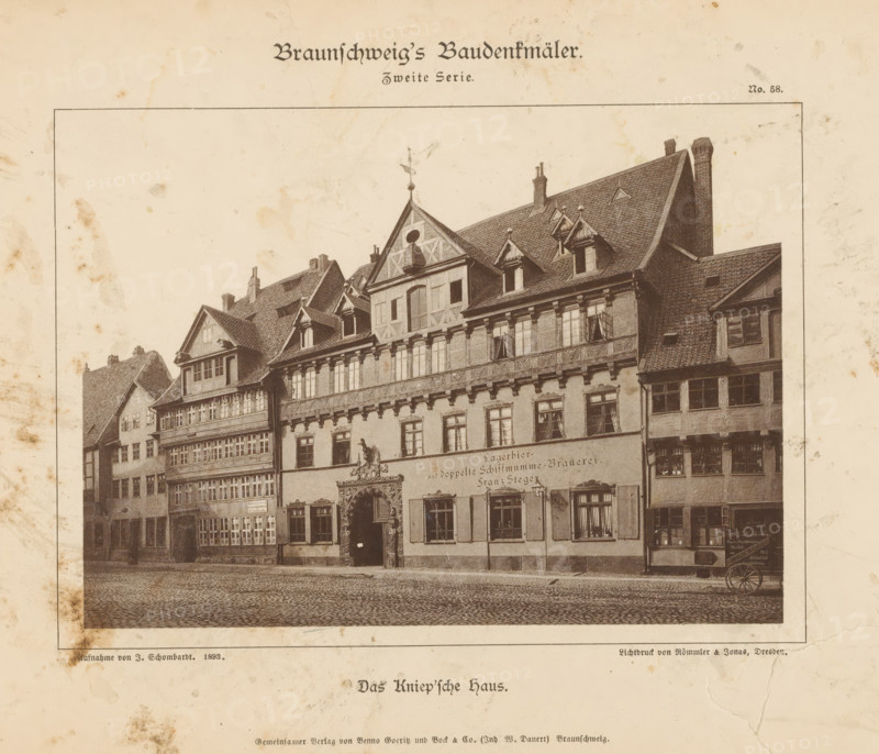Das Kniep'sche Haus, Exterior of a brewery in Braunschweig, Braunschweig's Baudenkmäler, page, photomechanical print, number: 'No. 58.', photographer: J. Schombardt, Braunschweig, cliché maker: Römmler & Jonas, Dresden, publisher: Benno und Wilhelm Danert Goeritz, 1893, Lower Saxony, Saxony, paper, collotype, photoprint, height 113 mm x width 155 mm, city-view in general, 'veduta', facade (of house or building), A sepia-toned print showing a row of ornate, historic buildings with steep gabled roofs, dormer windows, decorative timber framing, and a large carved entranceway; the street in front is paved with cobblestones and a small cart wheel is visible at the right edge; stains and foxing appear on the paper around the framed image and the paper shows a thin printed border.