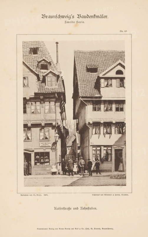 Kaiserstraße und Rehnstoben, View of the Kaiserstraße and the Rehnstoben in Braunschweig, Braunschweig's Baudenkmäler, page, photomechanical print, number: 'No. 63.', photographer: W. Berge, Braunschweig, cliché maker: Römmler & Jonas, Dresden, publisher: Benno und Wilhelm Danert Goeritz, 1893, W. Berge, Römmler & Jonas, Benno und Wilhelm Danert Goeritz, photographer, cliché maker, publisher, Lower Saxony, Saxony, paper, collotype, photoprint, height 149 mm x width 106 mm, street, lane, alley, facade (or house or building), A vertical sepia photograph shows two tall half-timbered buildings facing each other across a narrow cobblestone street, each with steep tiled roofs and multiple dormer windows; the left building has a shopfront with display windows and a hanging lantern, while the right building features shuttered windows and a doorway with a figure standing in the entrance; a group of people, including men, women, and children dressed in period clothing, stand and pose in the stre...