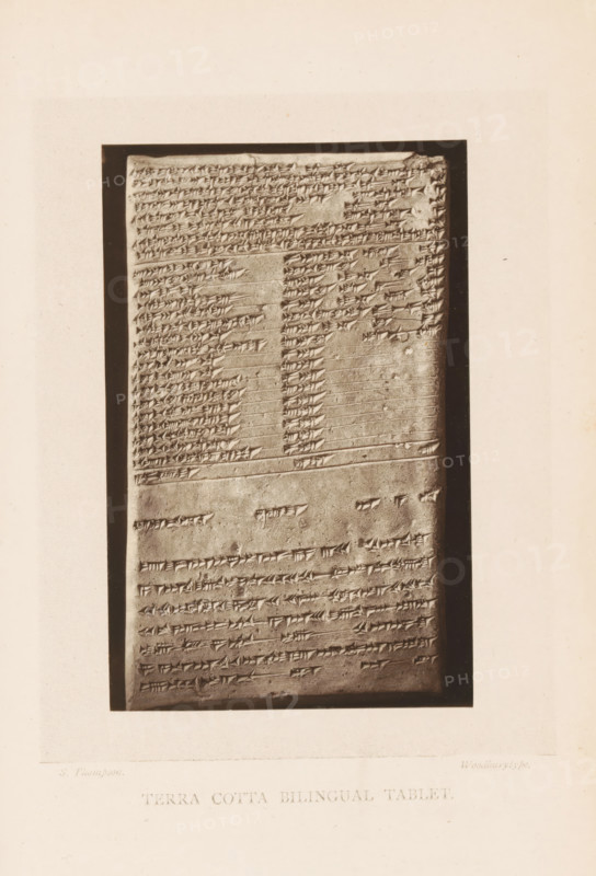 Terra cotta bilingual tablet, Clay tablet with bilingual inscription, page, photomechanical print, photographer: Stephen Thompson, c. 1871 - in or before 1876, paper, Woodburytype, height 121 mm x width 78 mm, excavation, archaeology, clay tablet, stone tablet, A vertical rectangular stone tablet with rows of incised wedge-shaped markings sits within a dark rectangular frame on a light background; the tablet surface shows horizontal lines separating sections and areas of denser and sparser markings, with some small chips and worn spots on the stone, and a narrow margin of the frame visible around the tablet.