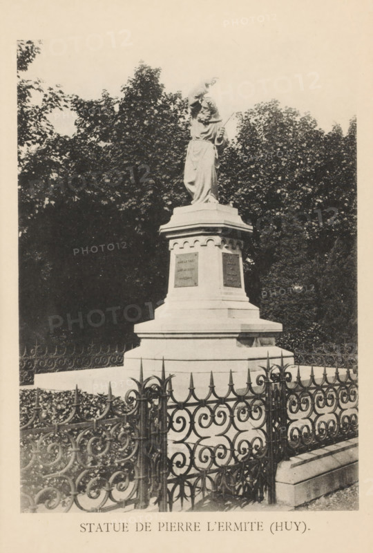 Statue de Pierre l'Ermite (Huy), Statue of Peter the Hermit in Huy, page, photomechanical print, photographer: attributed to Victor Gaillard, Huy, cliché maker: attributed to Emile Aubry, Brussels, c. 1885 - in or before 1890, Victor Gaillard, Emile Aubry, photographer, cliché maker, Hoei, Attributed to, paper, collotype, photoprint, height 144 mm x width 104 mm, Person, Petrus van Amiens, monument, statue, A stone statue of a robed figure stands on a multi-tiered pedestal surrounded by an ornate metal fence, with dense leafy trees filling the background and a pale sky above.