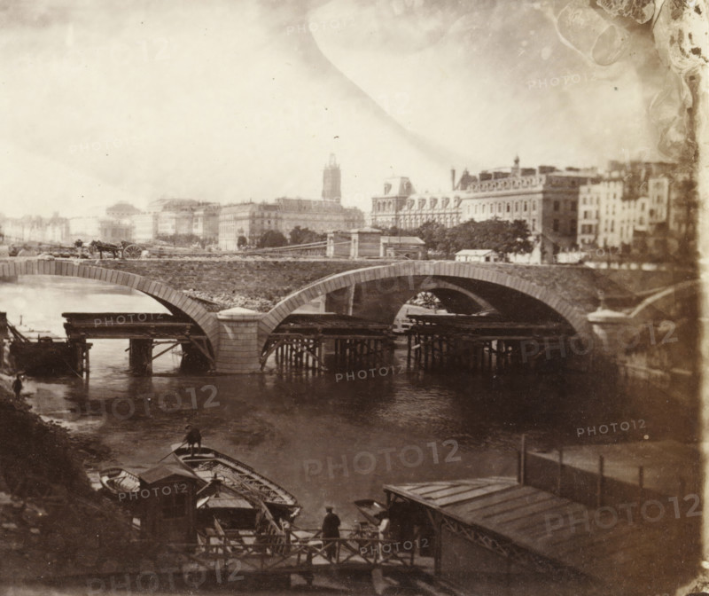 Construction of the Pont Louis-Philippe in Paris, stereograph, photographer: Charles Nègre, Paris, 1860 - 1862, paper, albumen print, albumen print from glass negative, height 82 mm x width 197 mm, river, bridge, Pont Louis-Philippe, A sepia-toned scene showing a stone arch bridge crossing a river with wooden scaffolding and pilings beneath some arches, small rowboats moored along the near bank, a person standing on a landing near the boats, another person in a small boat on the water, a cart with a horse and a driver on the bridge, distant multi-story buildings and trees along the far bank, and a cloudy sky above.