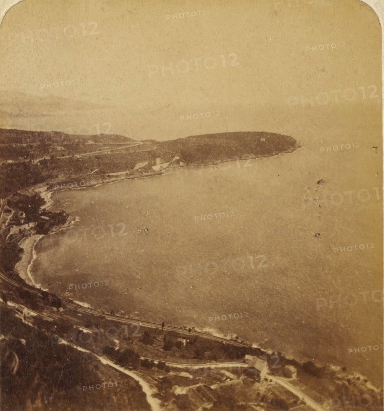 Cap Martin taken from the Corniche, France, View of the bay of Cap Martin, Views and landscapes in Europe, Africa and Asia, Geographical Sculpture Gallery, collected by MJ Broekhuijsen, Head of a school in Amsterdam, stereograph, Numbered 895 in the lower left corner of the photo., annotation: 'Cape and bay at the foot of the Maritime Alps, 20 km east of Nice. The cape is approximately 45 minutes' walk long., The picture was taken from the high road running from Nice to Genoa. (La Corniche)', Cap Martin, publisher: Merkelbach & Co., Amsterdam, compiler (person in literature): Martien Johan Broekhuijsen, c. 1905, Merkelbach & Co., Martien Johan Broekhuijsen, photographer, publisher, compiler (person in literature), Provence-Alpes-Côte d'Azur, pasteboard, paper, albumen print, height 89 mm x width 178 mm, Part of a group of 52 stereophotos used in primary education as a supplement to school charts. The entire series consisted of 274 items in 10 categories (A to K)., cape (coast), A sepia...